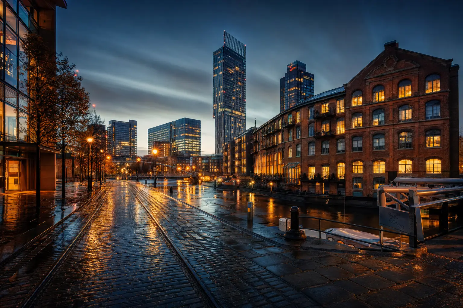 Dramatic aerial view of Manchester city centre at dusk, with lit office buildings and streets reflecting in rain-wet roads